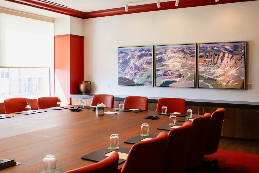 Modern conference room with wooden table, red chairs, and landscape paintings.