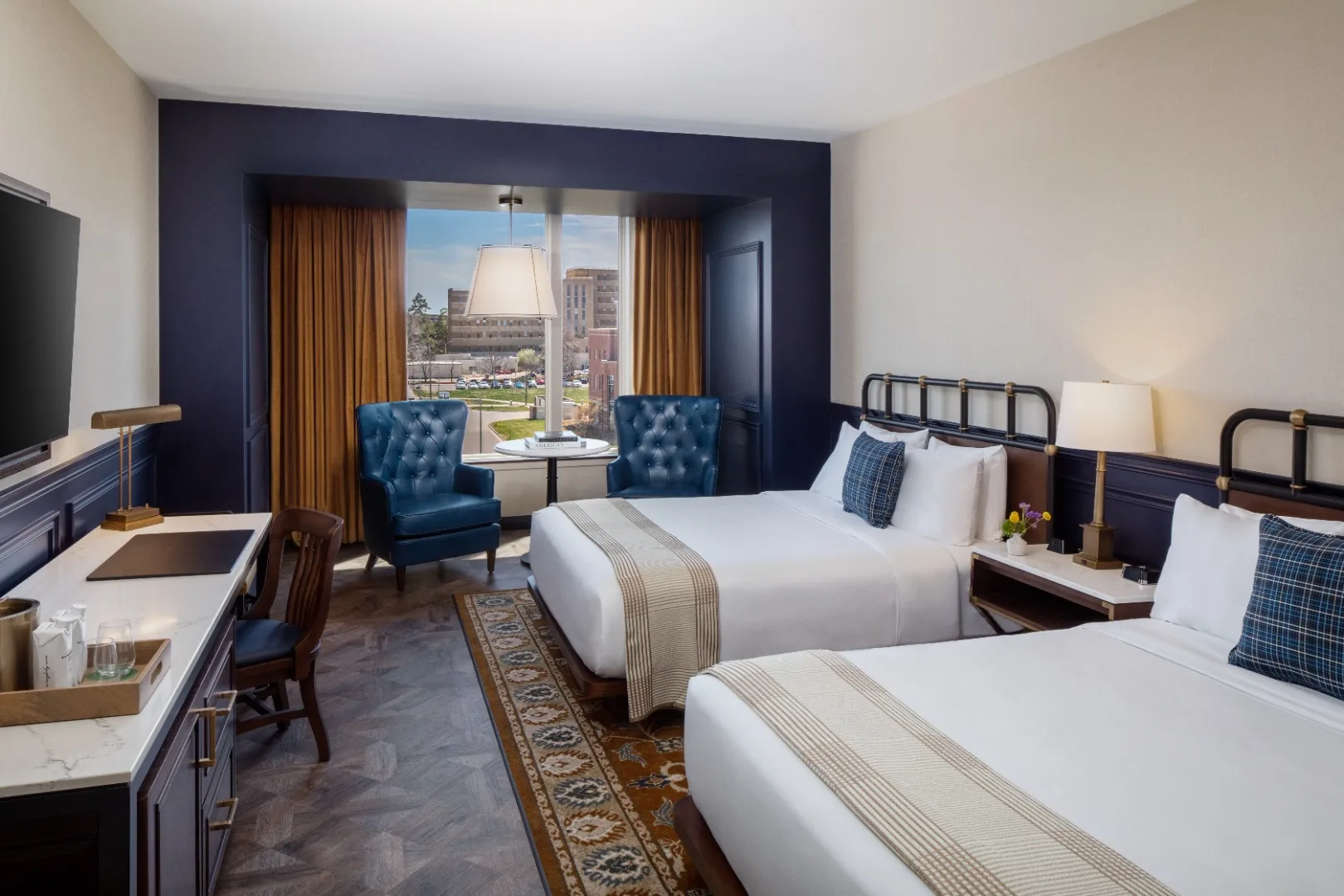 Hotel room with two beds, blue armchairs, and city view