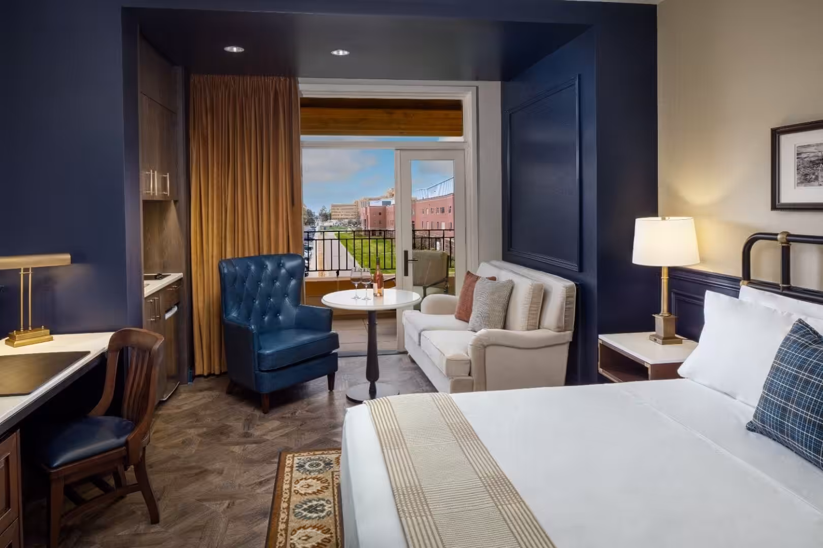 Hotel room with king bed, blue armchair, and balcony view at The Benson Hotel & Faculty Club.