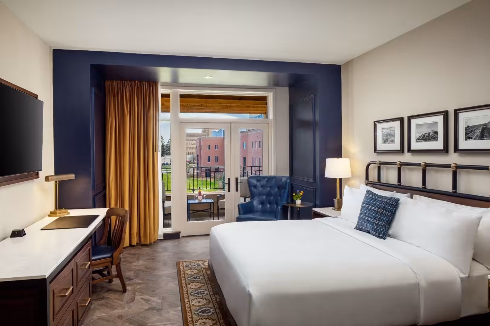 Modern hotel room with king bed, blue accent wall, and balcony overlooking a brick building.
