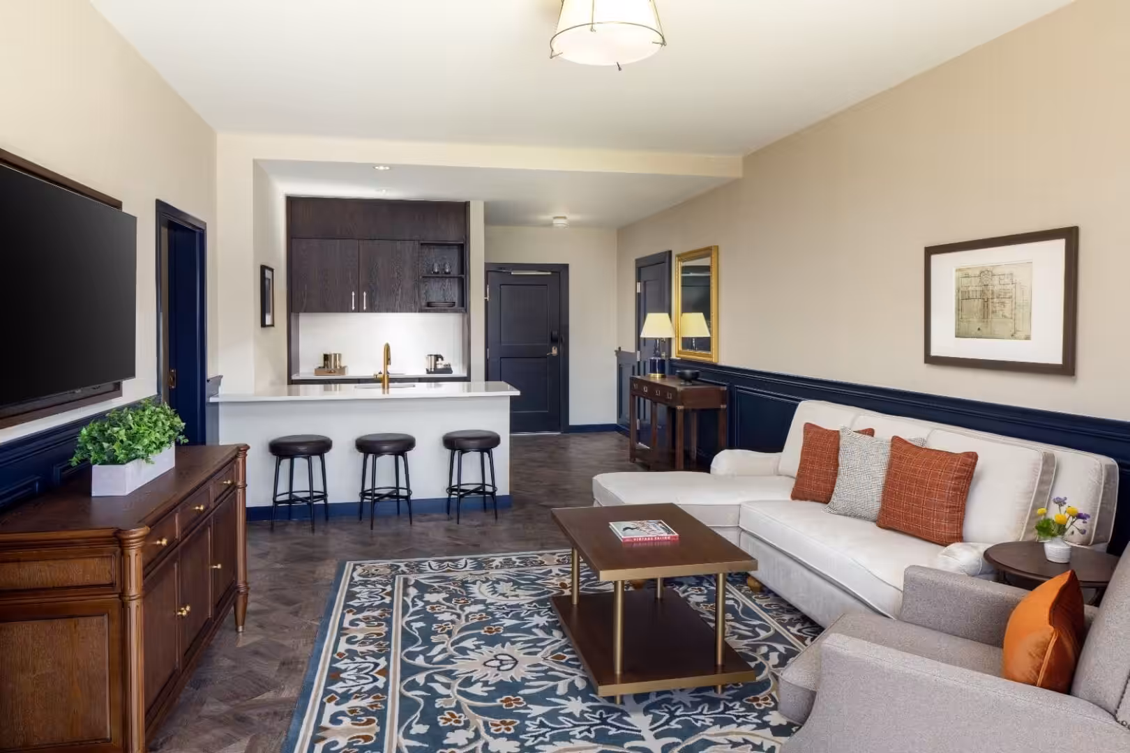 Spacious hotel suite living area with sectional sofa, kitchenette, and flat-screen TV.