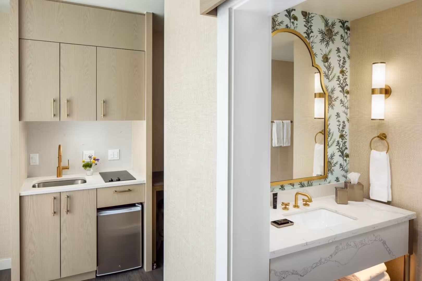 Modern hotel suite kitchenette with light wood cabinetry and marble bathroom vanity featuring botanical wallpaper.