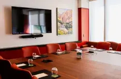 Modern conference room with wooden table, red chairs, wall-mounted TV, and landscape painting.
